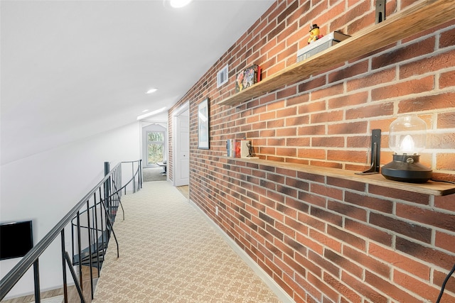 corridor with visible vents, an upstairs landing, carpet, brick wall, and lofted ceiling