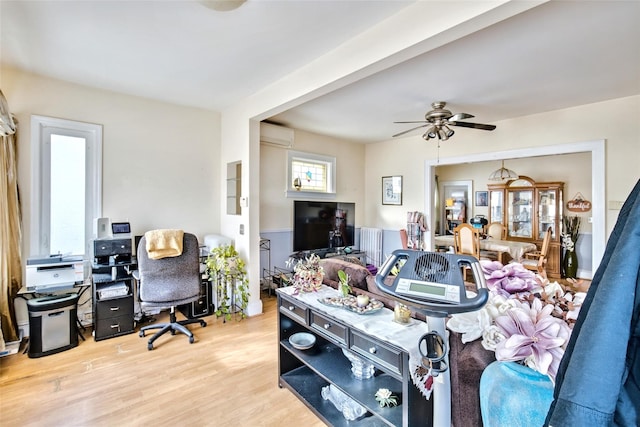 living room featuring a wall unit AC, light wood finished floors, and a ceiling fan