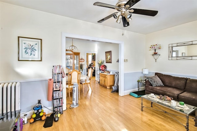 living room with baseboards, radiator heating unit, a ceiling fan, and light wood-style floors