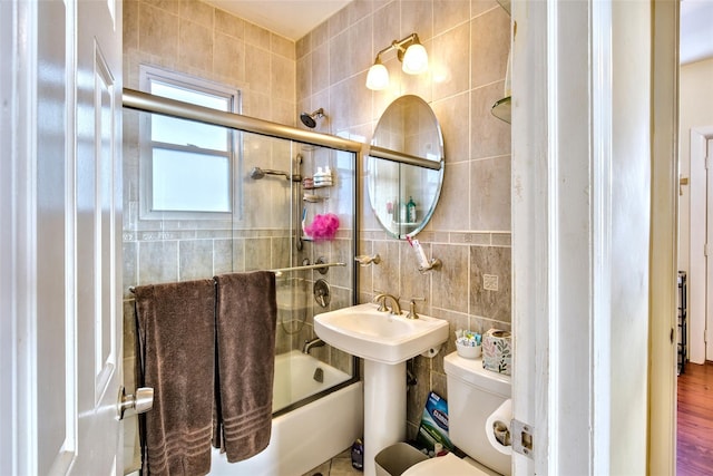 full bath featuring toilet, shower / bath combination with glass door, a sink, and tile walls