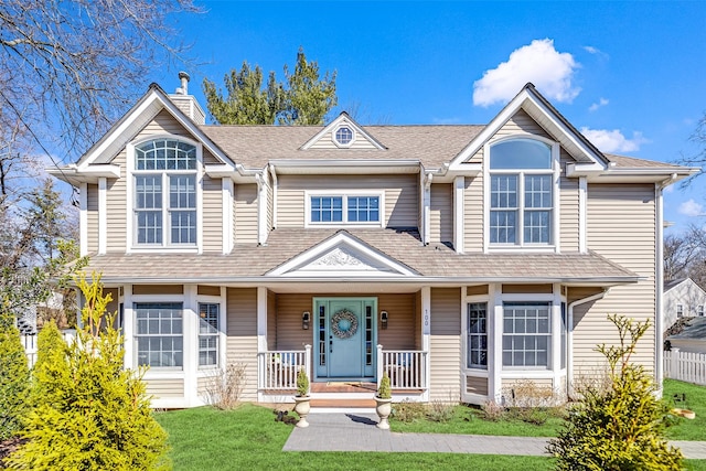 view of front facade featuring covered porch, a shingled roof, a chimney, and a front lawn