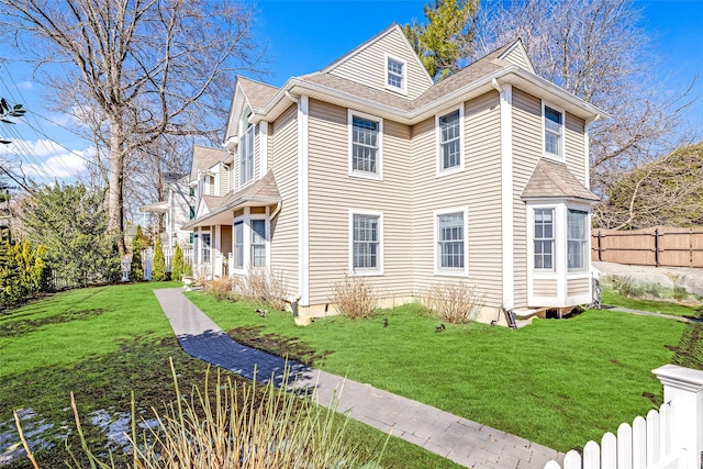 view of side of property with a yard, a shingled roof, and fence