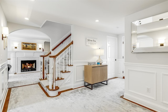 entrance foyer featuring a wainscoted wall, recessed lighting, a decorative wall, stairway, and a lit fireplace