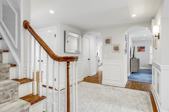 foyer with stairway, arched walkways, a decorative wall, and wood finished floors