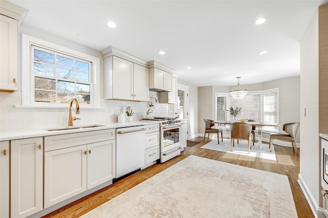 kitchen featuring white dishwasher, wood finished floors, a sink, range with gas stovetop, and tasteful backsplash