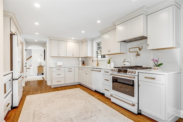 kitchen with white appliances, arched walkways, light wood-style flooring, light countertops, and a sink