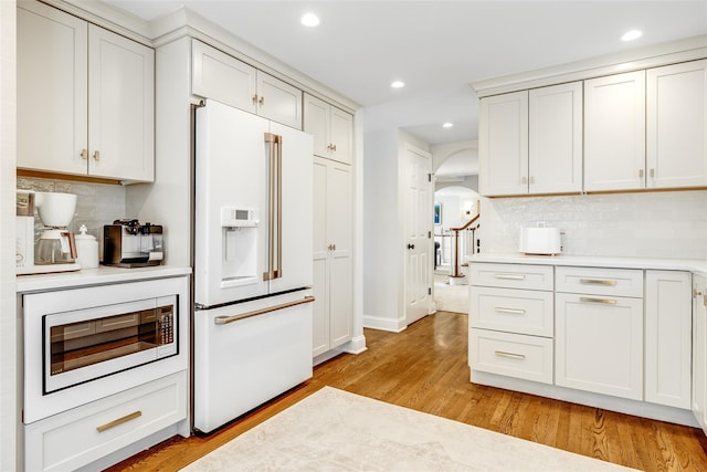 kitchen featuring arched walkways, high end fridge, light countertops, light wood-type flooring, and built in microwave