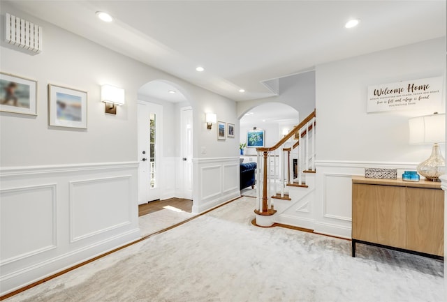 foyer featuring arched walkways, a decorative wall, recessed lighting, wood finished floors, and stairway