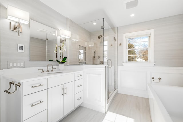 full bathroom featuring a tub to relax in, a decorative wall, a wainscoted wall, vanity, and a stall shower