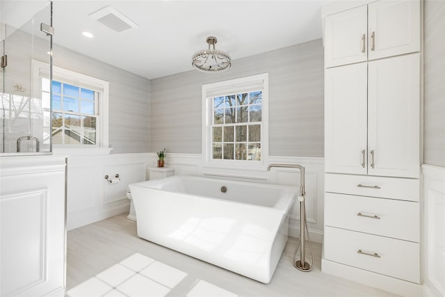 full bathroom with wainscoting, a soaking tub, a shower stall, and visible vents