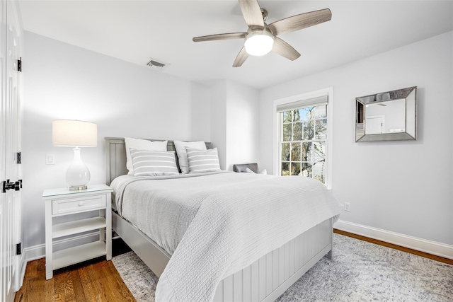 bedroom with ceiling fan, wood finished floors, visible vents, and baseboards