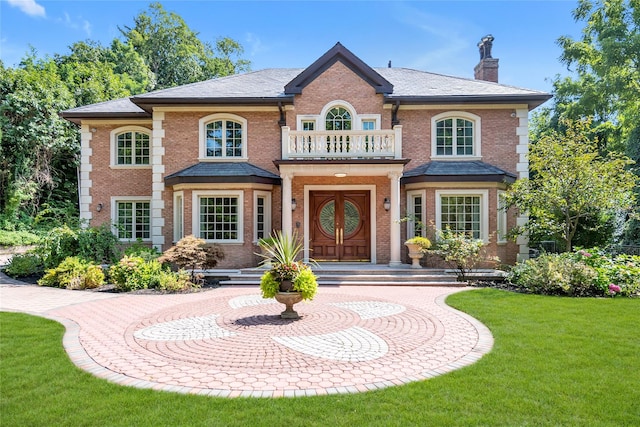 colonial home featuring a balcony, a chimney, a front lawn, and brick siding