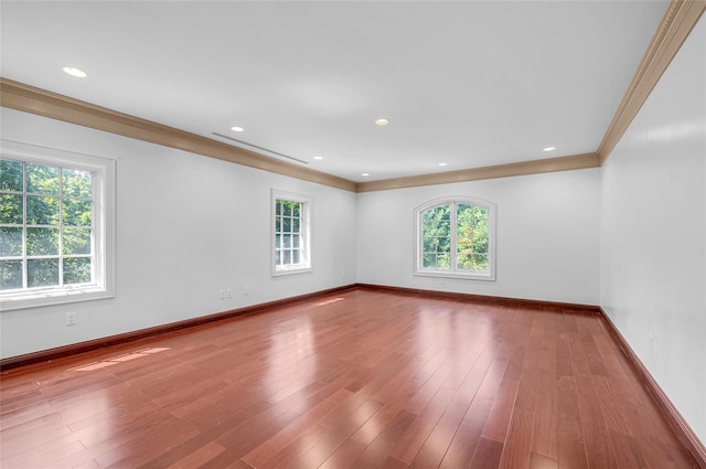 empty room featuring a wealth of natural light, ornamental molding, and wood finished floors