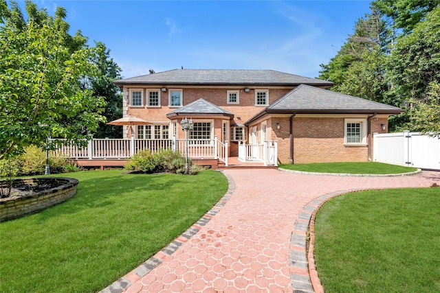 back of property featuring a wooden deck, fence, a lawn, and brick siding