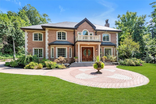 colonial house with a chimney, brick siding, a balcony, and a front lawn