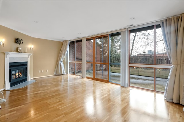 unfurnished living room featuring wood finished floors, a wall of windows, a fireplace with flush hearth, and baseboards