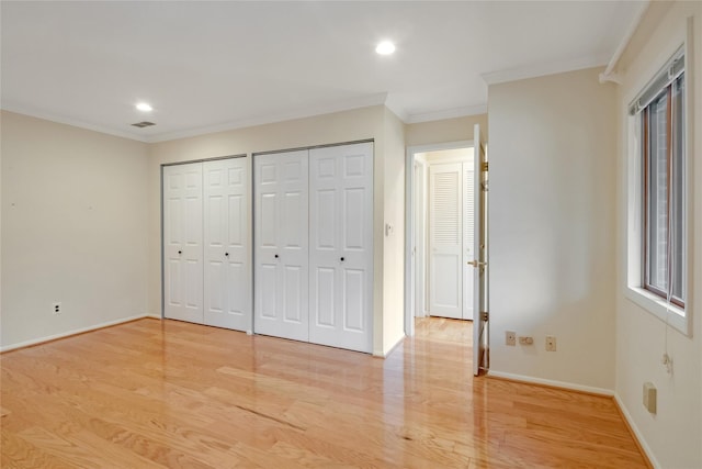 unfurnished bedroom with ornamental molding, light wood-style floors, baseboards, and multiple closets