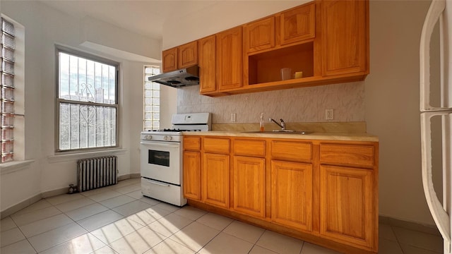 kitchen with radiator, white gas range, light countertops, under cabinet range hood, and a sink