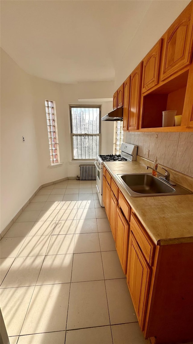 kitchen with light tile patterned floors, under cabinet range hood, a sink, white range with gas cooktop, and light countertops