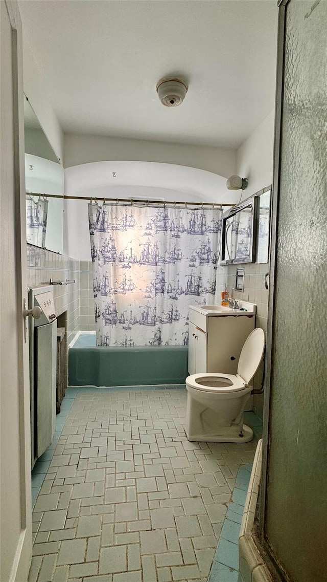 bathroom featuring toilet, vanity, brick floor, shower / bathtub combination, and tile walls