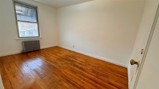 empty room with baseboards, radiator heating unit, and wood finished floors