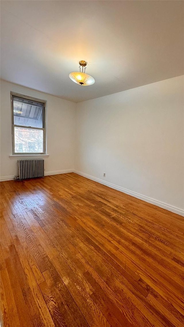 empty room featuring radiator heating unit, wood finished floors, and baseboards