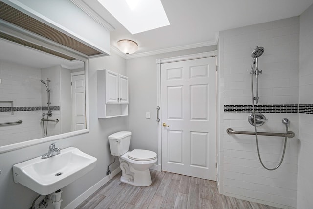 full bathroom with a skylight, crown molding, a sink, a tile shower, and wood finished floors