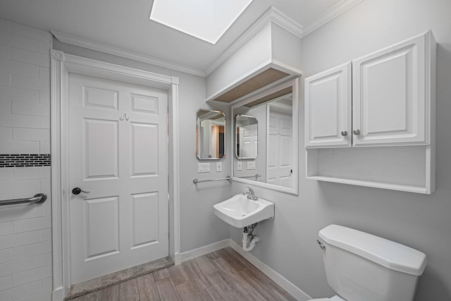 bathroom featuring a skylight, crown molding, baseboards, and wood finished floors