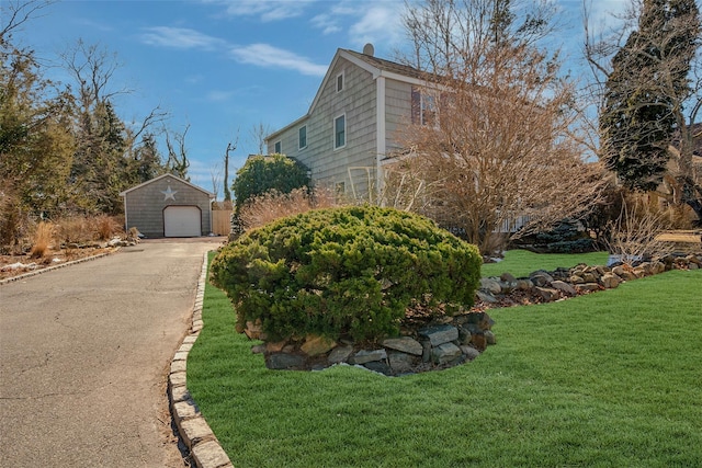 view of side of home featuring aphalt driveway, a lawn, an outdoor structure, and a detached garage