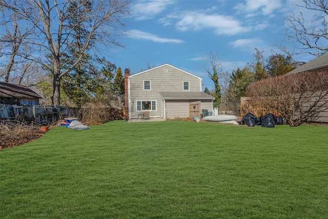 back of house featuring a chimney, fence, and a lawn