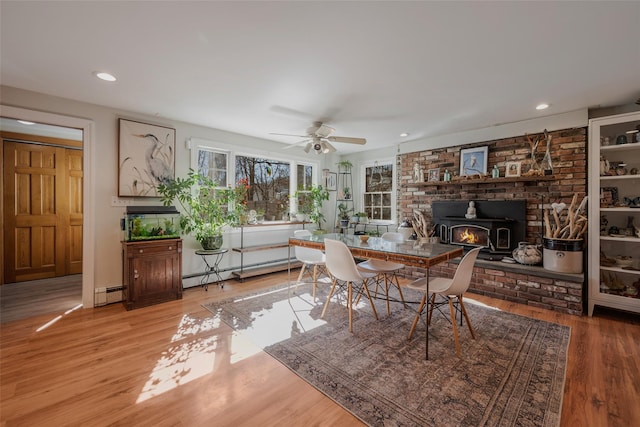 dining space featuring a wood stove, a baseboard radiator, wood finished floors, and recessed lighting