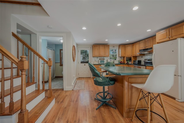 kitchen featuring a center island, white appliances, light wood-style flooring, and a breakfast bar area