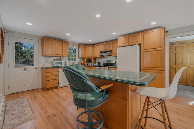 kitchen with white appliances, light wood-style floors, a kitchen island, under cabinet range hood, and a kitchen bar