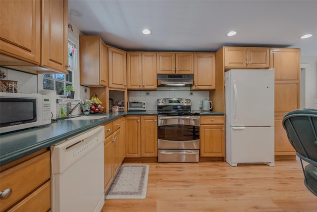 kitchen with dark countertops, light wood-style floors, a sink, white appliances, and under cabinet range hood