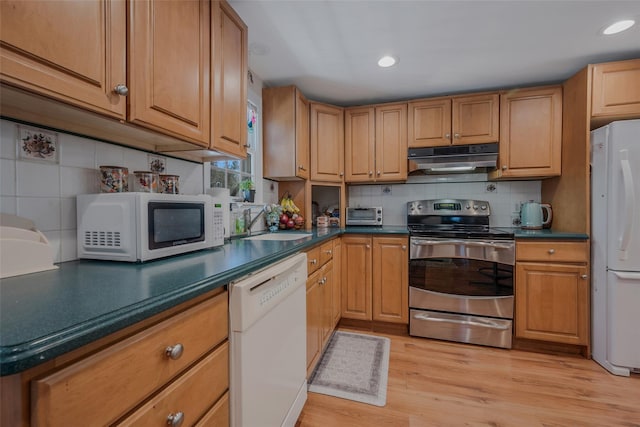 kitchen featuring white appliances, light wood-style floors, dark countertops, under cabinet range hood, and a sink