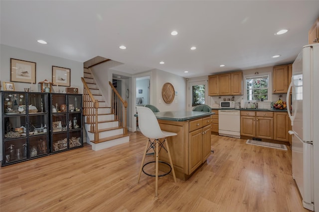 kitchen with dark countertops, white appliances, a kitchen island, and light wood finished floors