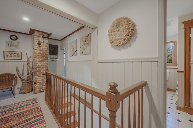 hall with a wainscoted wall, an upstairs landing, and crown molding