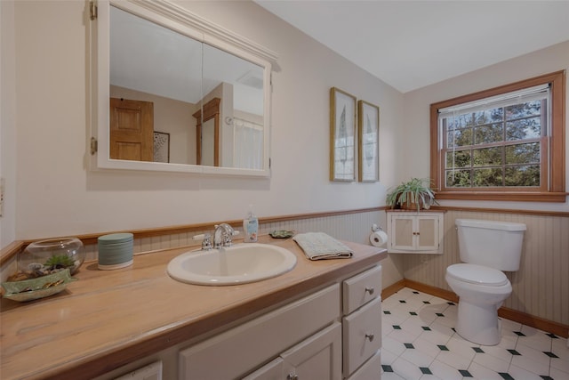 bathroom featuring toilet, vanity, vaulted ceiling, and wainscoting