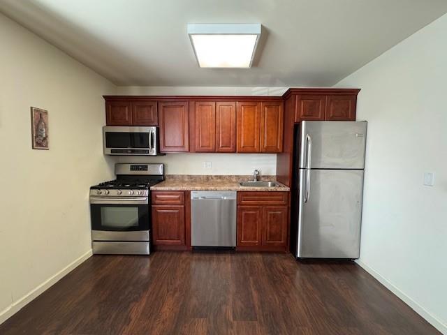 kitchen with dark wood-type flooring, baseboards, stainless steel appliances, and a sink