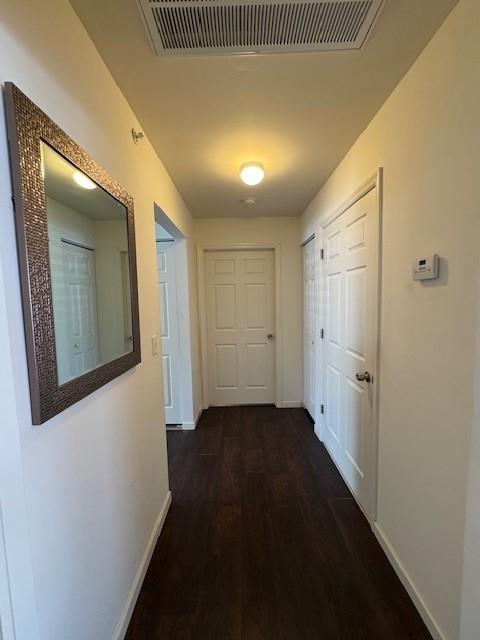 corridor featuring visible vents, dark wood finished floors, and baseboards