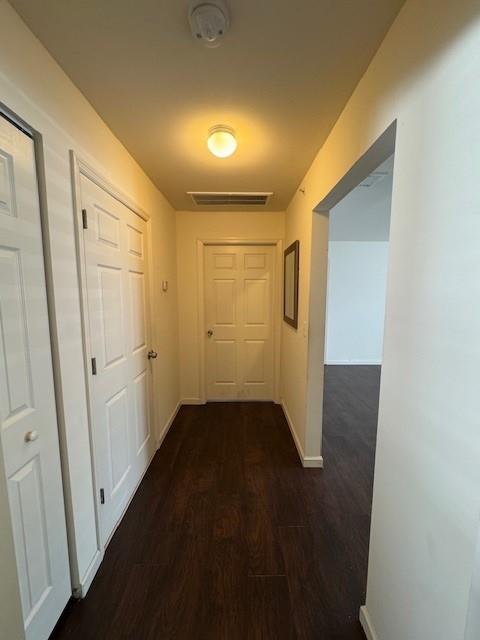 hall featuring dark wood-style flooring, visible vents, and baseboards