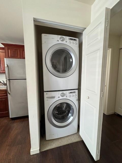 laundry room with stacked washing maching and dryer, laundry area, dark wood-style floors, and a sink