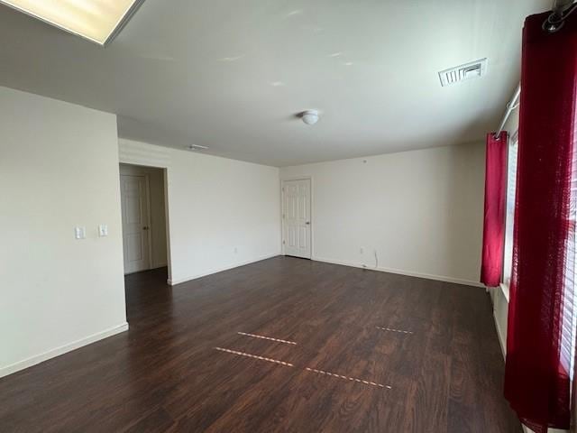 empty room featuring dark wood-style floors, visible vents, and baseboards