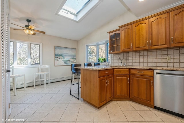 kitchen with vaulted ceiling with skylight, light tile patterned flooring, a baseboard heating unit, stainless steel dishwasher, and brown cabinets