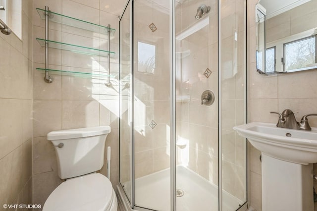 full bath with toilet, a shower stall, a sink, and tile walls