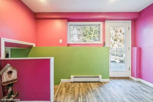 interior space featuring a baseboard heating unit, wood finished floors, and baseboards