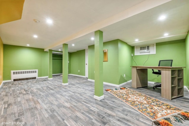 finished basement with recessed lighting, a wall mounted air conditioner, radiator heating unit, and wood finished floors