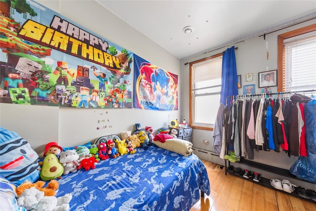 bedroom with multiple windows, a baseboard heating unit, and wood finished floors