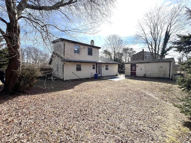 back of house with an outbuilding, a patio area, and a chimney