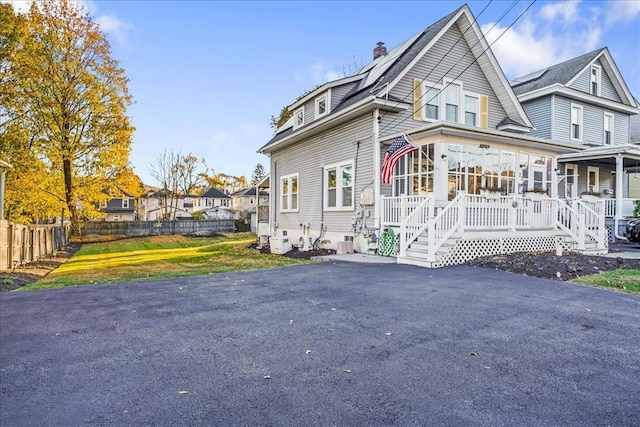 view of front of house with covered porch, a chimney, fence, and a front yard